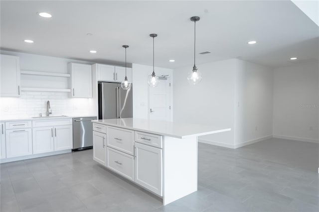 kitchen with a kitchen island, sink, white cabinets, decorative light fixtures, and appliances with stainless steel finishes