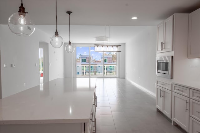 kitchen with stainless steel microwave, white cabinets, decorative light fixtures, and a kitchen island