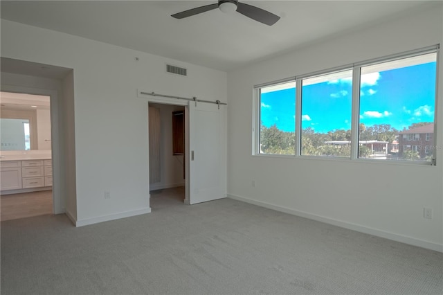 unfurnished bedroom with connected bathroom, a barn door, multiple windows, and ceiling fan