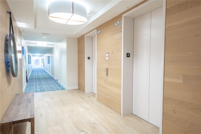 hall featuring light hardwood / wood-style flooring, wood walls, and elevator