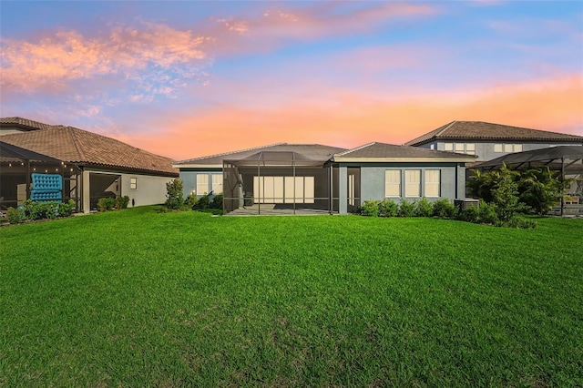 back house at dusk with a patio, a lawn, and glass enclosure