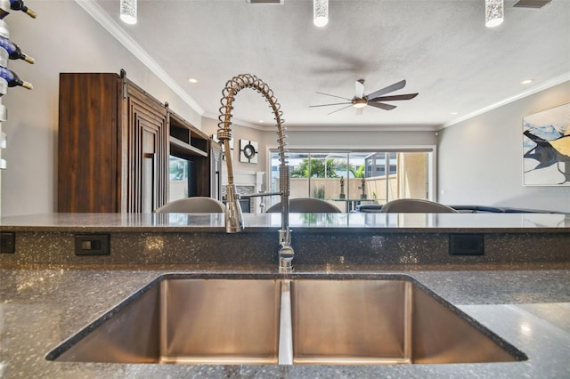 kitchen with dark stone countertops, crown molding, and sink