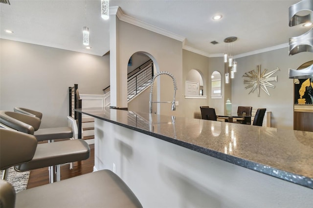 kitchen featuring ornamental molding, dark stone countertops, hardwood / wood-style flooring, and hanging light fixtures