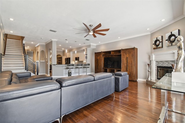 living room with crown molding, a tiled fireplace, ceiling fan, and dark hardwood / wood-style flooring