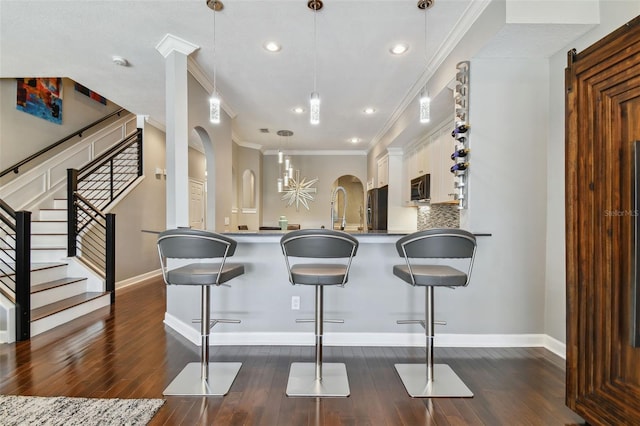 kitchen with a breakfast bar area, white cabinetry, black appliances, dark wood-type flooring, and pendant lighting