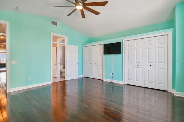 unfurnished bedroom featuring multiple closets, dark wood-type flooring, ensuite bath, vaulted ceiling, and ceiling fan