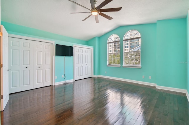 unfurnished bedroom with dark hardwood / wood-style flooring, lofted ceiling, two closets, and ceiling fan