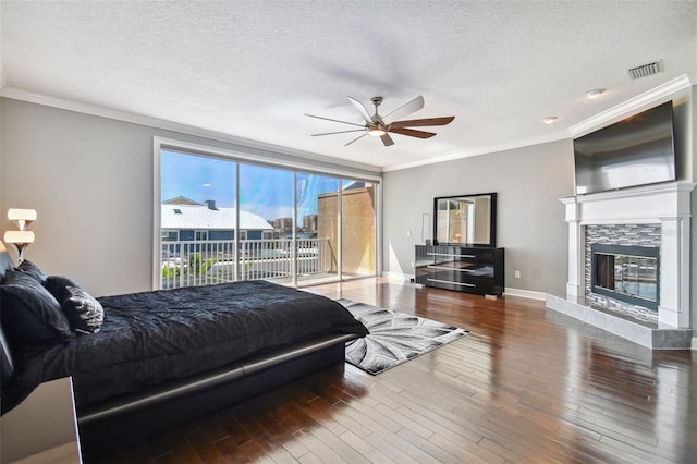 bedroom featuring access to outside, hardwood / wood-style floors, a textured ceiling, a fireplace, and ceiling fan