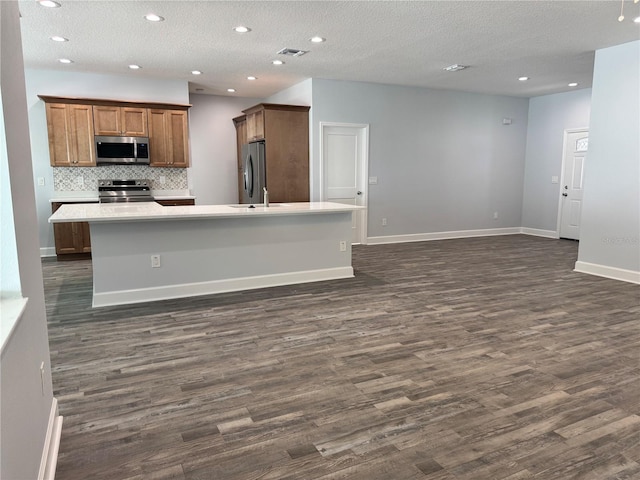 kitchen featuring appliances with stainless steel finishes, a center island with sink, and dark wood-type flooring