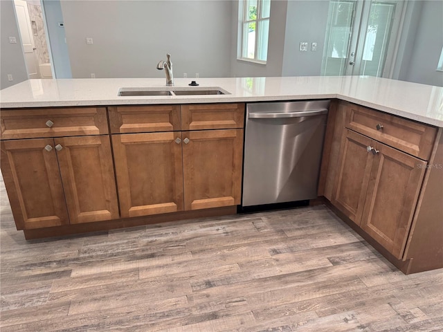 kitchen featuring dishwasher, light stone countertops, light wood-type flooring, and sink