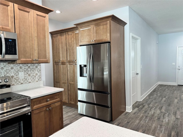 kitchen featuring dark wood-type flooring, light stone counters, a textured ceiling, decorative backsplash, and appliances with stainless steel finishes