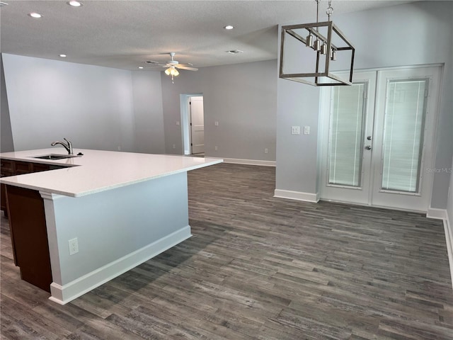 kitchen with sink, dark wood-type flooring, hanging light fixtures, an island with sink, and ceiling fan with notable chandelier