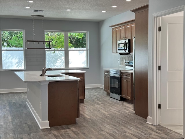 kitchen featuring a center island with sink, sink, a textured ceiling, light stone counters, and stainless steel appliances