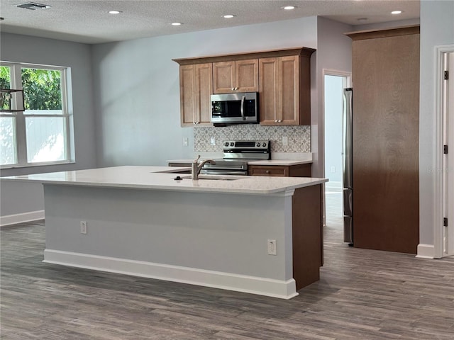 kitchen featuring dark hardwood / wood-style flooring, stainless steel appliances, and an island with sink