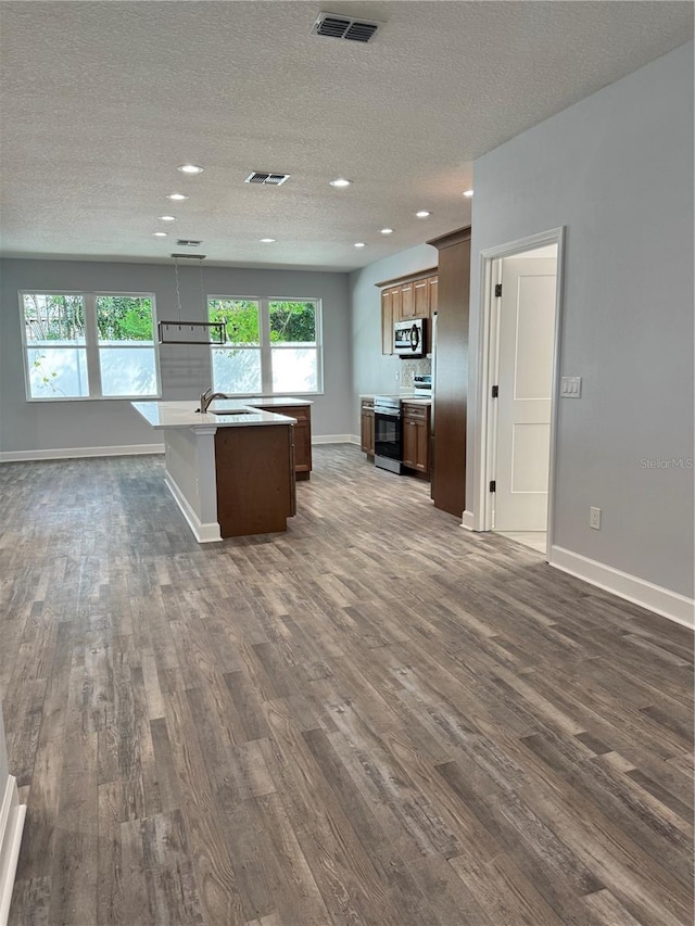 kitchen featuring appliances with stainless steel finishes, a center island with sink, a wealth of natural light, and dark hardwood / wood-style floors