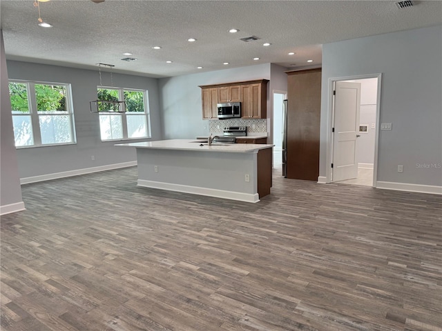 kitchen with backsplash, dark hardwood / wood-style floors, a kitchen island with sink, and appliances with stainless steel finishes