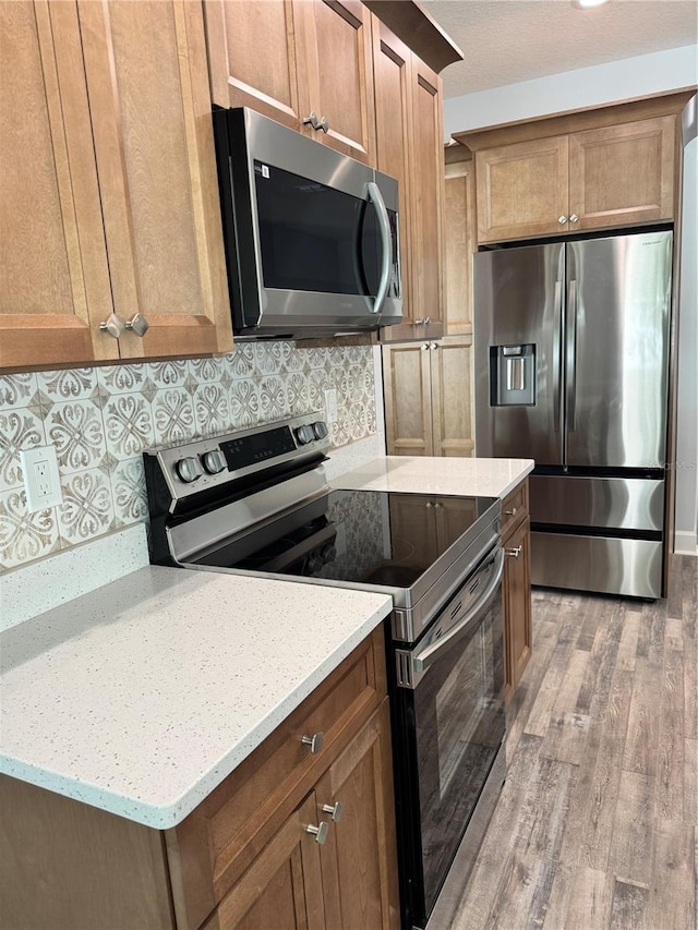 kitchen with decorative backsplash, appliances with stainless steel finishes, light wood-type flooring, and light stone counters