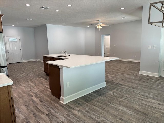 kitchen with dark hardwood / wood-style flooring, a textured ceiling, ceiling fan, sink, and a center island with sink