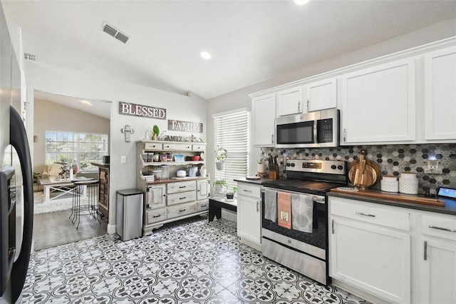 kitchen with appliances with stainless steel finishes, lofted ceiling, white cabinets, and backsplash