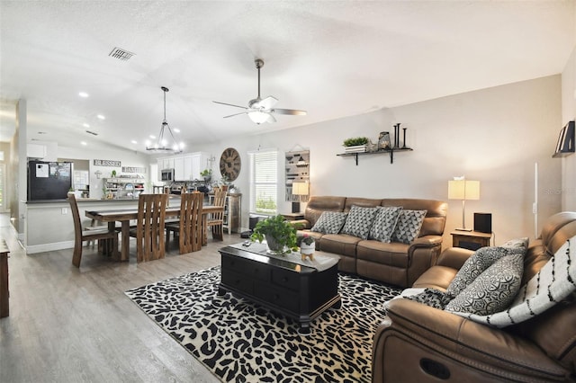 living room with light hardwood / wood-style floors, vaulted ceiling, and ceiling fan with notable chandelier