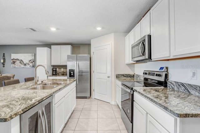 kitchen with stainless steel appliances, a center island with sink, wine cooler, sink, and white cabinets