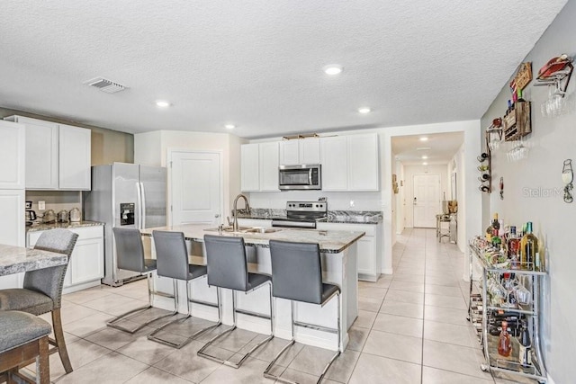 kitchen with a kitchen island with sink, a kitchen bar, stainless steel appliances, and white cabinetry