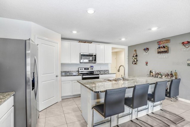 kitchen with a kitchen island with sink, a breakfast bar area, white cabinets, appliances with stainless steel finishes, and light stone counters