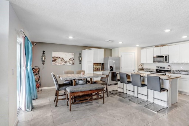 kitchen with a kitchen breakfast bar, a center island with sink, white cabinetry, light tile patterned floors, and appliances with stainless steel finishes