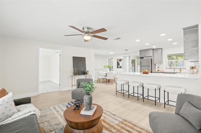 living room with light hardwood / wood-style flooring, sink, and ceiling fan