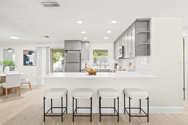 kitchen with gray cabinetry, kitchen peninsula, stainless steel appliances, decorative backsplash, and light hardwood / wood-style flooring