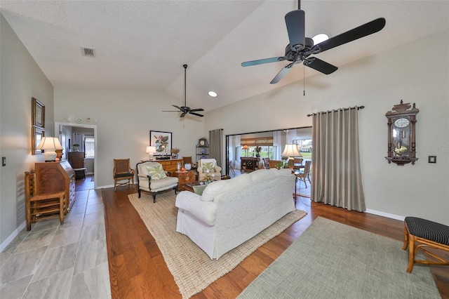 living room with a textured ceiling, ceiling fan, light hardwood / wood-style floors, and vaulted ceiling