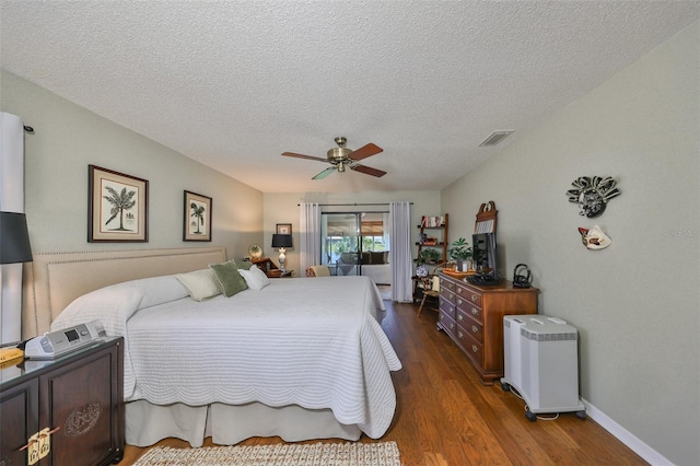 bedroom with ceiling fan, dark hardwood / wood-style floors, a textured ceiling, and access to outside