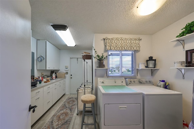 clothes washing area with washer and dryer, light wood-type flooring, a textured ceiling, and cabinets