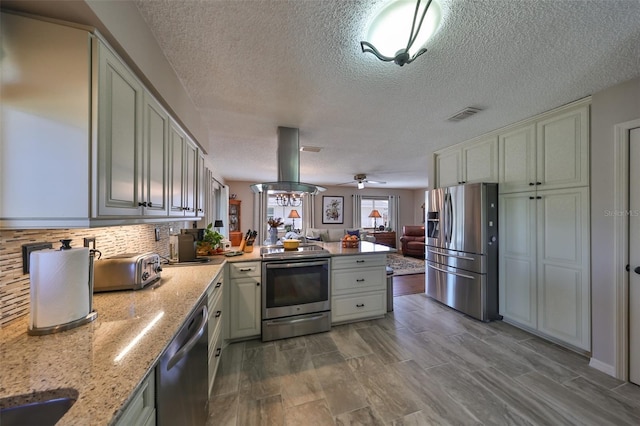 kitchen featuring ceiling fan, appliances with stainless steel finishes, island range hood, light stone counters, and kitchen peninsula