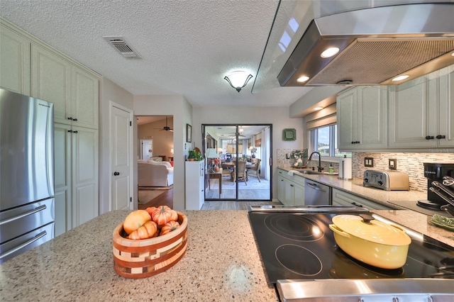 kitchen with appliances with stainless steel finishes, backsplash, a textured ceiling, ceiling fan, and wall chimney range hood