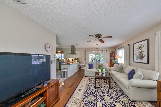 living room featuring hardwood / wood-style floors, ceiling fan with notable chandelier, and a textured ceiling