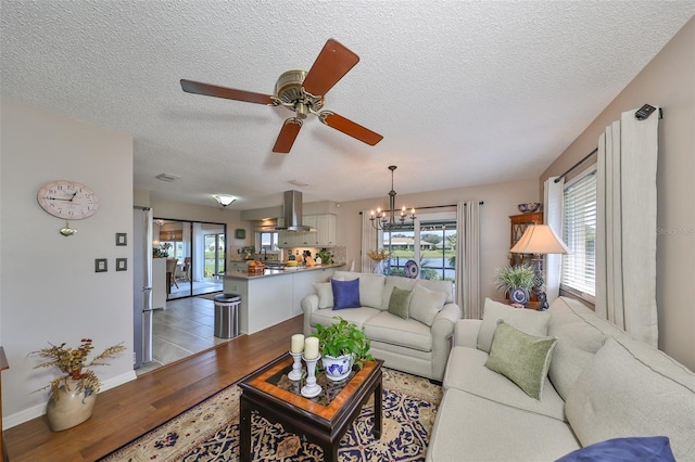 living room featuring ceiling fan with notable chandelier, a textured ceiling, and light hardwood / wood-style floors