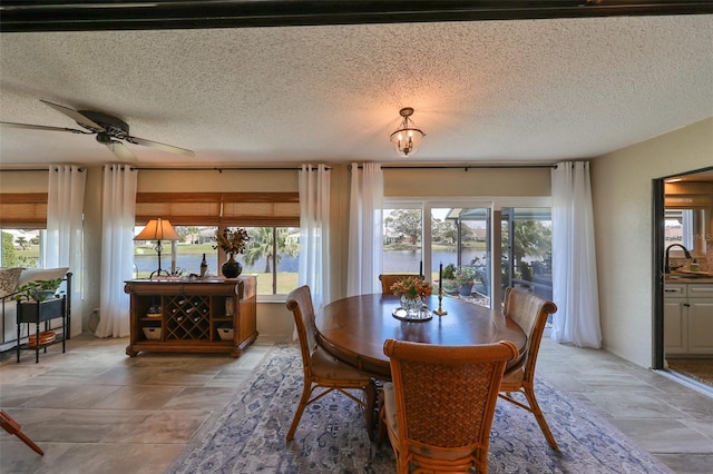 dining space with ceiling fan, sink, a textured ceiling, and a water view