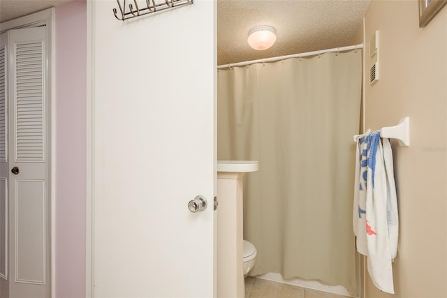 bathroom with toilet, a textured ceiling, and tile patterned floors