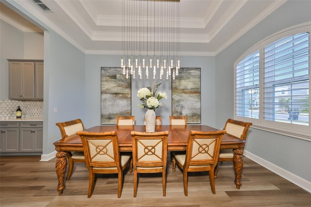 dining space featuring crown molding, a tray ceiling, and light hardwood / wood-style flooring