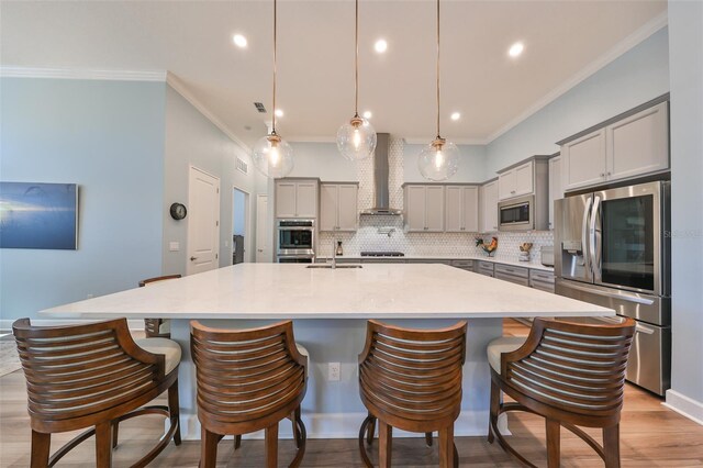 kitchen featuring wall chimney range hood, a spacious island, appliances with stainless steel finishes, gray cabinetry, and decorative light fixtures