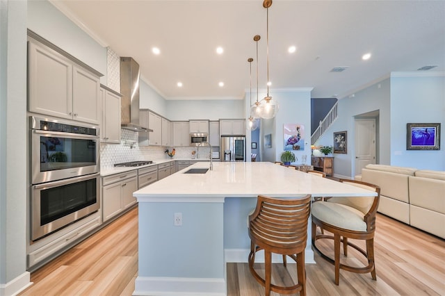 kitchen with wall chimney exhaust hood, a breakfast bar area, hanging light fixtures, light wood-type flooring, and appliances with stainless steel finishes