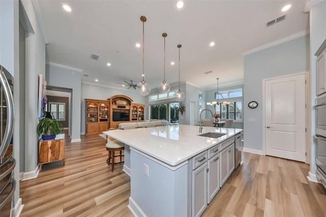 kitchen with light hardwood / wood-style flooring, hanging light fixtures, a center island with sink, ornamental molding, and sink