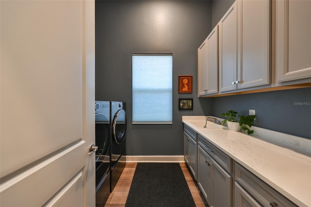 laundry room featuring cabinets, independent washer and dryer, sink, and light hardwood / wood-style flooring