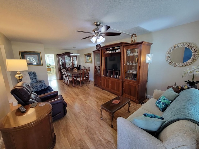 living room featuring light hardwood / wood-style flooring, a textured ceiling, and ceiling fan