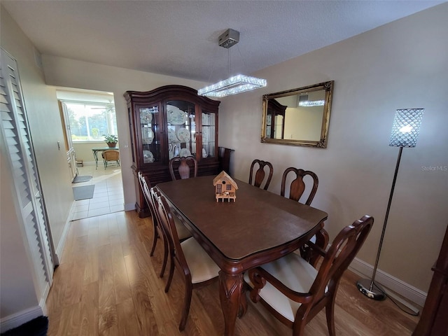 dining area featuring light hardwood / wood-style flooring, a textured ceiling, and a notable chandelier