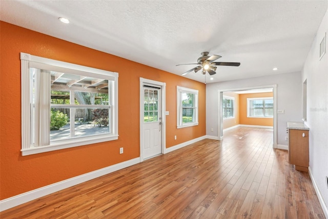 unfurnished living room featuring ceiling fan, a textured ceiling, a wealth of natural light, and light hardwood / wood-style flooring