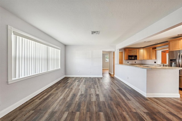 kitchen featuring dark hardwood / wood-style flooring, kitchen peninsula, stainless steel fridge, a textured ceiling, and light brown cabinetry