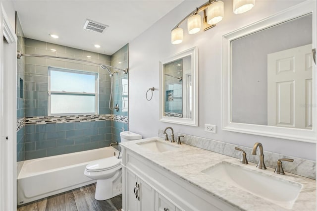 full bathroom featuring hardwood / wood-style flooring, tiled shower / bath combo, toilet, and vanity