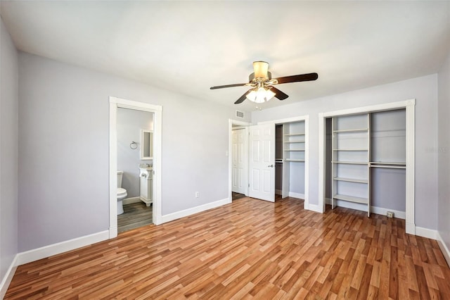 unfurnished bedroom featuring connected bathroom, ceiling fan, two closets, and light wood-type flooring